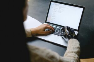 Mulher mexendo no computador com uma mão robótica.