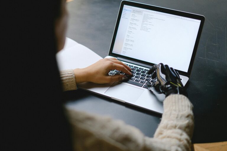 Mulher mexendo no computador com uma mão robótica.